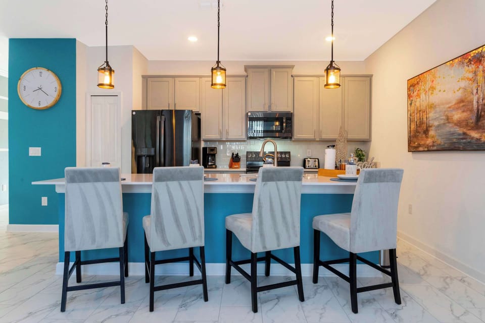 Pull up a stool at the vibrant breakfast bar! The bold teal accent wall and modern seating create a fun, contemporary vibe for family gatherings.