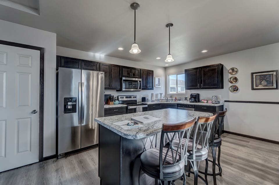 Kitchen with full complement of stainless steel appliances, cookware, bakeware, and large dining room table with seating for 8-10 people. 