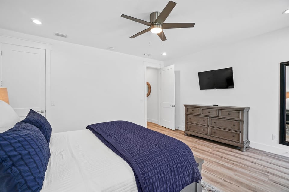 Unwind in your serene bedroom featuring a plush bed with navy accents, modern ceiling fan, and entertainment center for cozy evenings.