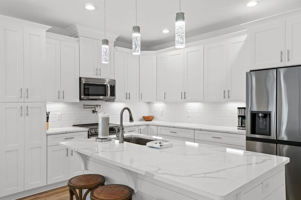 Your gourmet kitchen gleams with pristine white marble, stainless steel appliances, and sparkling pendant lights - perfect for preparing memorable meals together.