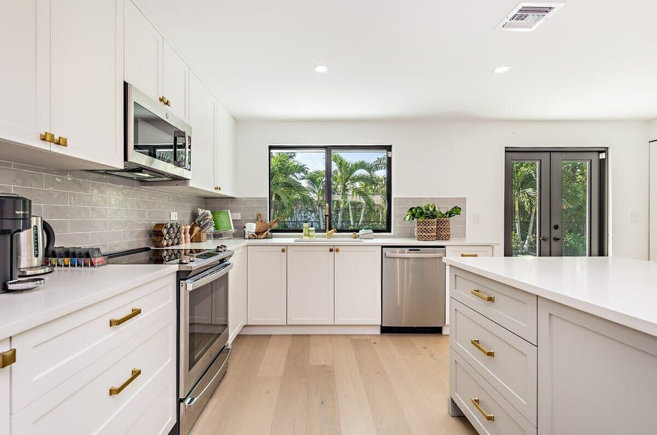 Modern kitchen with white cabinetry, stainless steel appliances, and natural light from garden-facing windows.