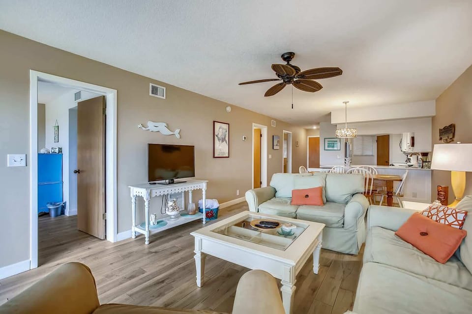 - View highlights the cozy living area with sofas, flat screen TV, and accent tables
- Neutral tones with pops of coral create a welcoming and stylish atmosphere
- Easy flow to the dining and kitchen areas keeps everyone connected