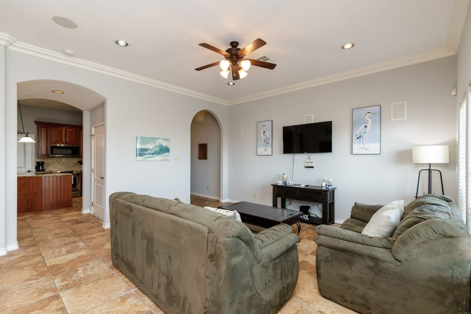 Relax in your spacious living room featuring plush seating, ocean-inspired artwork, and an open layout connecting to the kitchen.