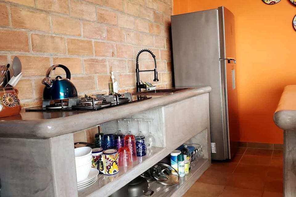 The open design kitchen features a full size refrigerator with automatic ice maker and cold water dispenser, hand hammered copper sink, 4-burner gas stove top, plenty of glassware, plates and cookware.