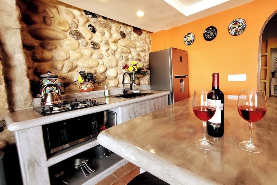 The kitchen features a concrete center island for food prep or dining and entertaining. Full size refrigerator with ice maker, 4-burner gas stove, microwave, toaster oven, coffee maker, professional quality cookware, and hand-hammered copper sink.