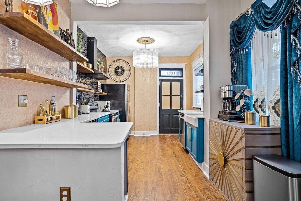 Cook in style at The Luxe with bold blue cabinetry, gold hardware, and open shelving that brings modern elegance to this fully stocked kitchen.