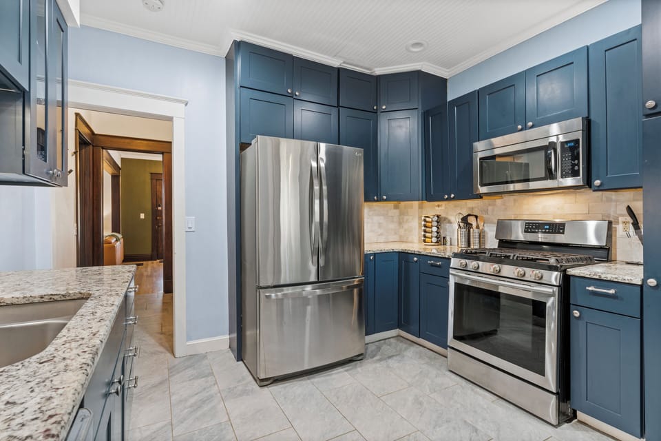 First-Floor Full Kitchen with stainless steel appliances, stunning blue cabinetry, and granite countertops—perfect for cooking at home between outings to Westport and West 39th Street’s walkable dining scene.