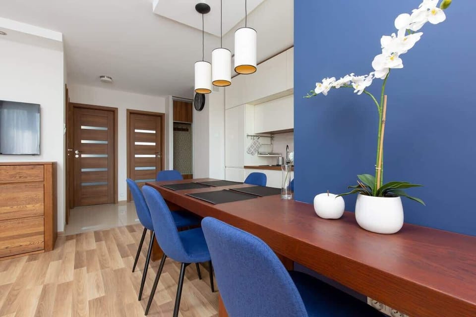A dining area featuring a wooden table and blue chairs, positioned near a window for plenty of light. The decor is simple yet elegant.