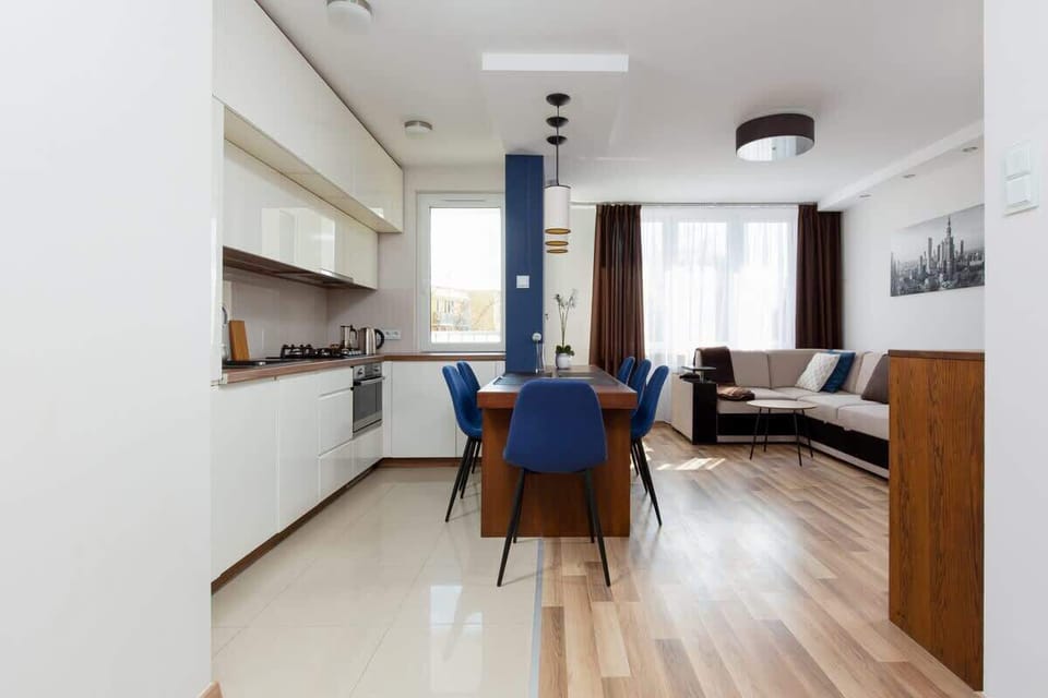 A wider view showing the living room and kitchen together, highlighting the open-plan layout. The wooden flooring ties the spaces together seamlessly.