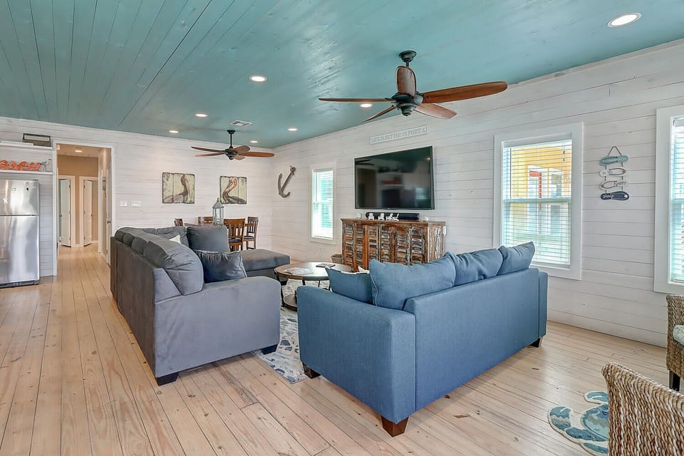 Relax in your coastal-inspired living room with plush blue sofas and warm wood floors beneath a stunning aqua ceiling.
