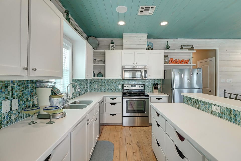 Step into your coastal-inspired kitchen where turquoise tile backsplash meets pristine white counters, creating the perfect space for your morning coffee ritual.
