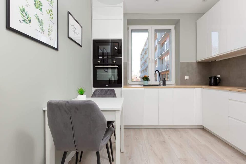 A sleek white kitchen with handleless cabinets, modern appliances, and a light wooden countertop.