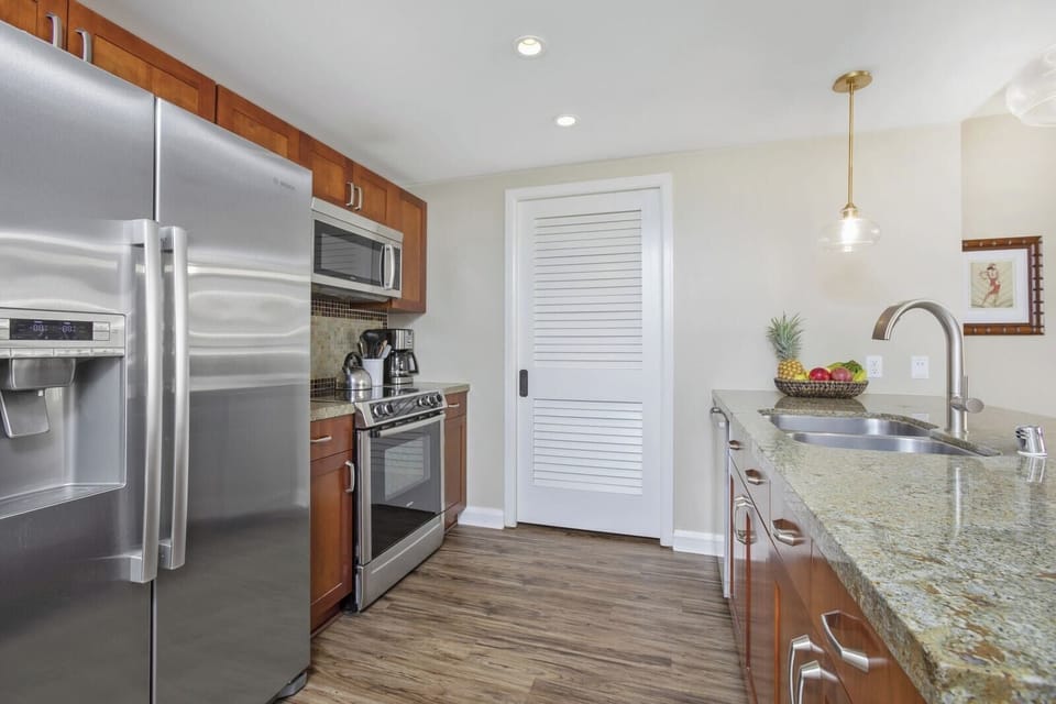 Contemporary kitchen features granite counters, stainless appliances, and tropical fruit basket.