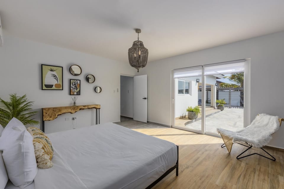 This bedroom has a king-size bed, an elegant chandelier, and a large sliding door that leads outside. It is air-conditioned and has comfortable seating as well as a console table.