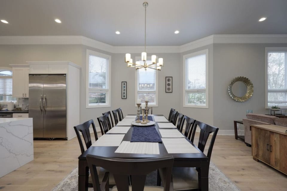 Dining room with a long dark table, black chairs, chandelier, and large windows