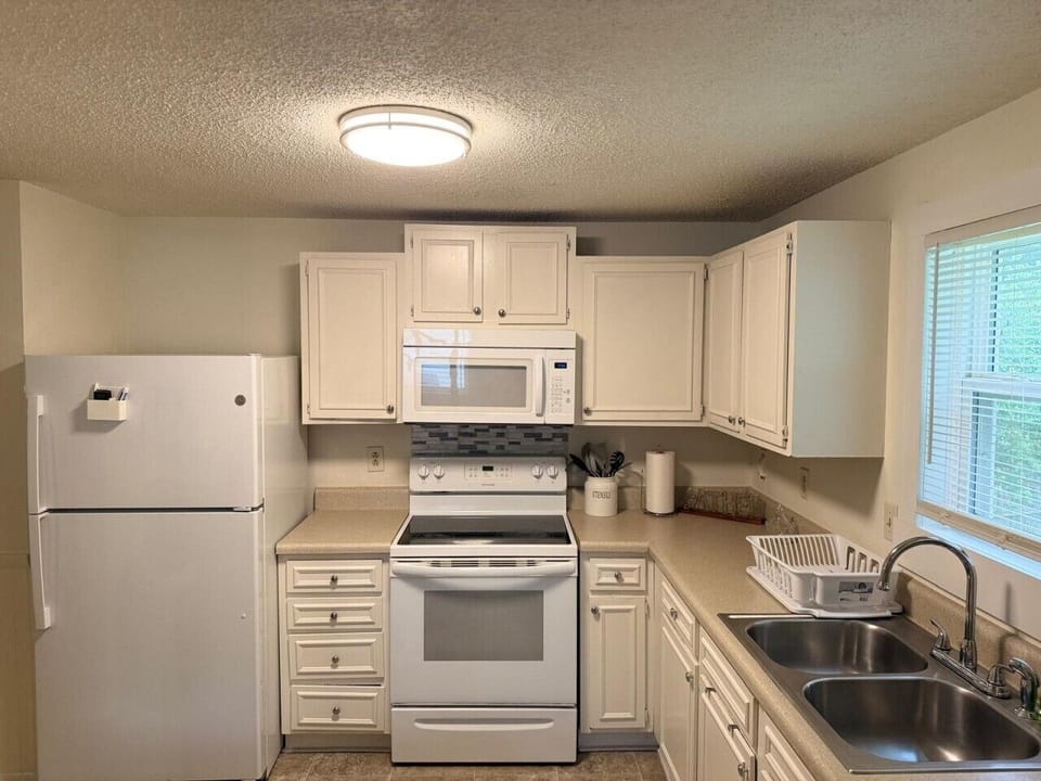 Fully equipped white kitchen with full-size refrigerator, electric stove, microwave — everything you need to cook real meals at home.