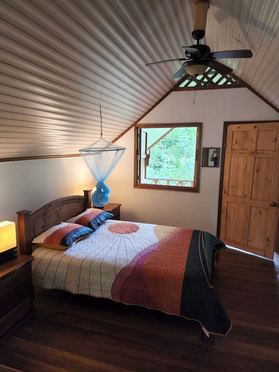 Queen bed, ceiling fan, mosquito net, and window towards private balcony outside