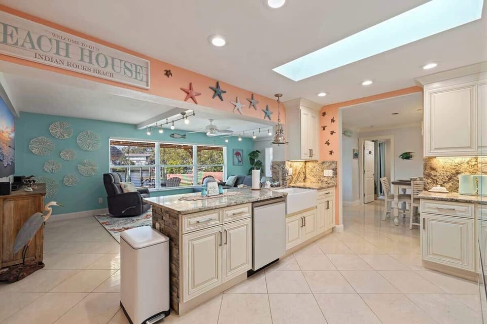 Open, airy coastal kitchen and living space filled with natural light. White cabinetry, granite countertops, skylights, and playful beach décor create a bright gathering spot perfect for cooking, relaxing, and enjoying time together by the water.