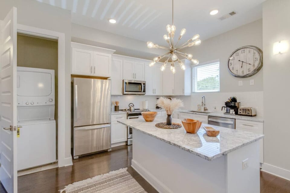 Stunning gourmet kitchen featuring white cabinetry, stainless steel appliances, a marble island, and an elegant sputnik chandelier.