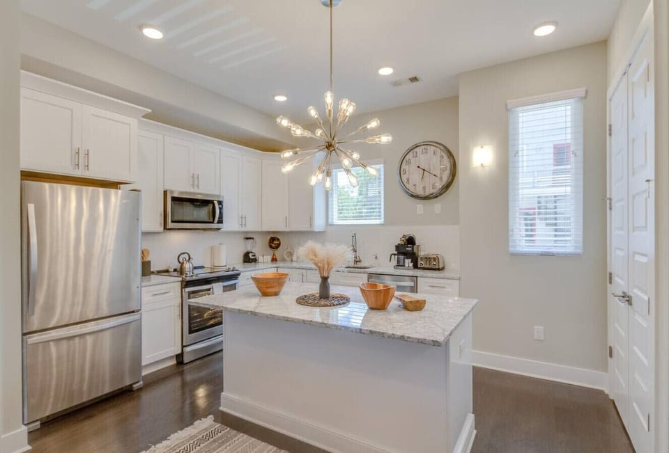 Modern kitchen space with white cabinetry, a marble-topped island, stainless appliances, and a decorative wall clock.