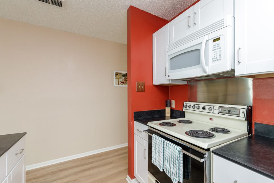 Your fully equipped kitchen features white appliances, sleek countertops, and vibrant red accents that create a cheerful cooking space.