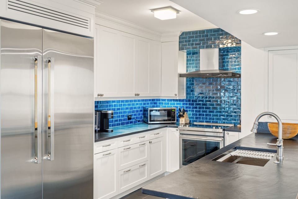 Step into your gourmet kitchen with stunning blue tile backsplash, stainless steel appliances, and spacious countertops perfect for cooking.