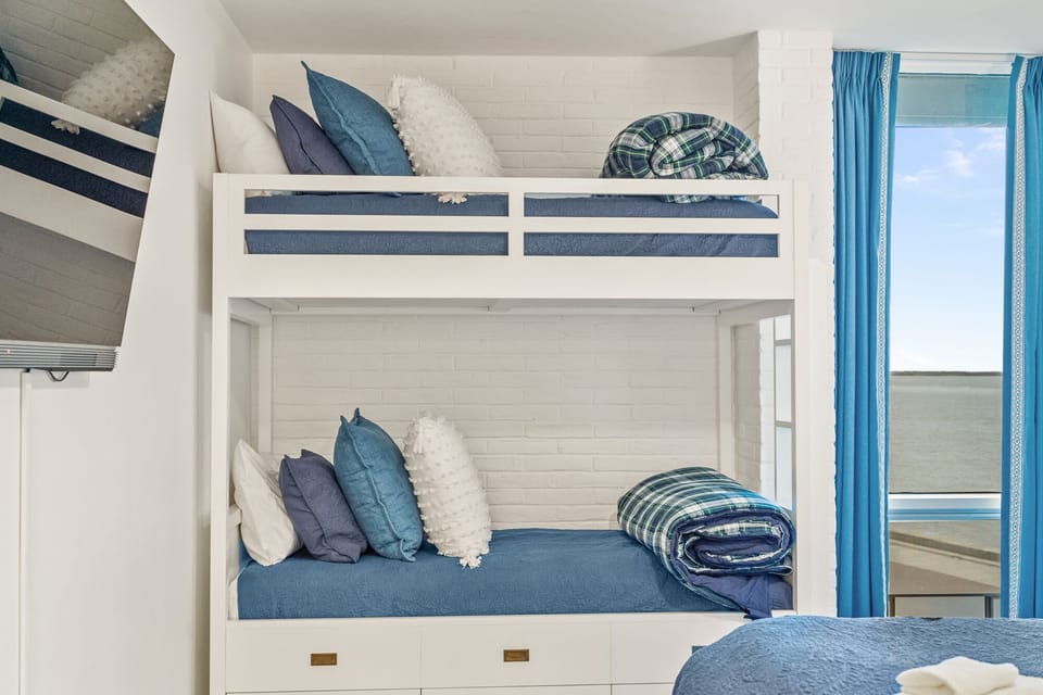 Cozy built-in bunks with soft blue linens and ocean views create your perfect seaside retreat.