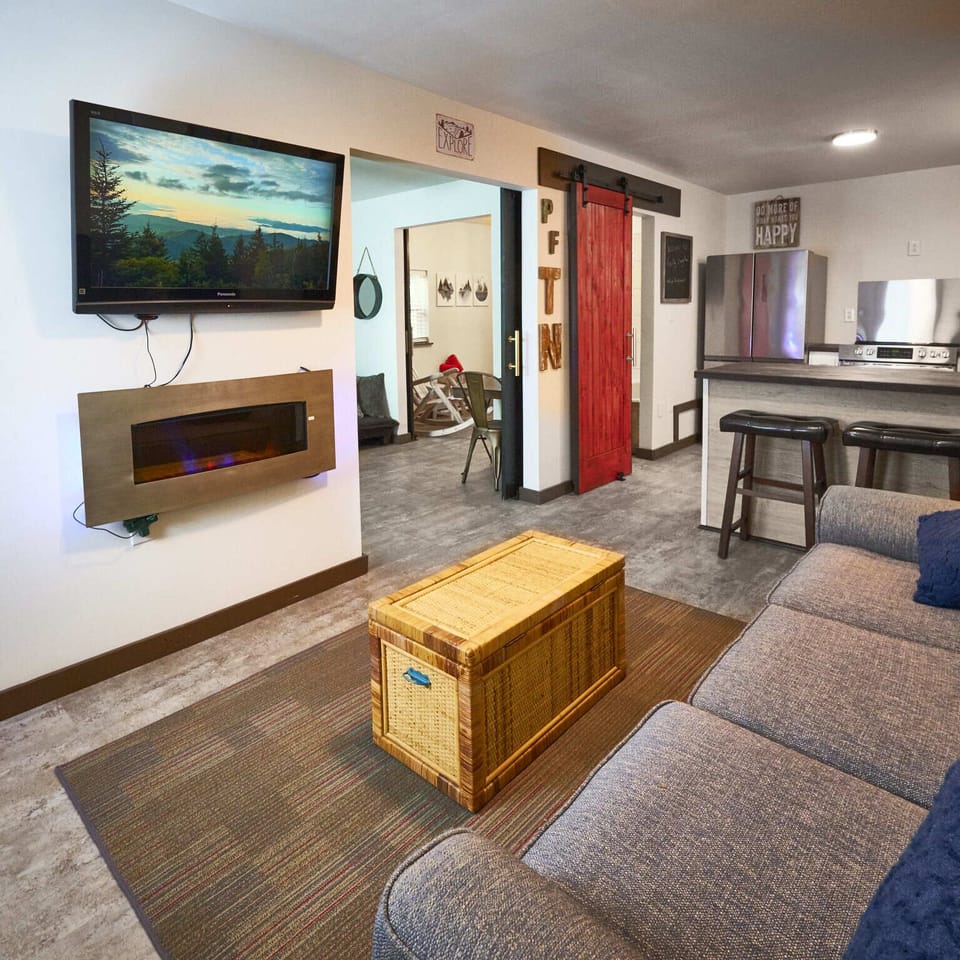 The living room has a mist-gray sofa bed, a coffee table, an electric fireplace, and a large wall-mounted flat-screen TV.