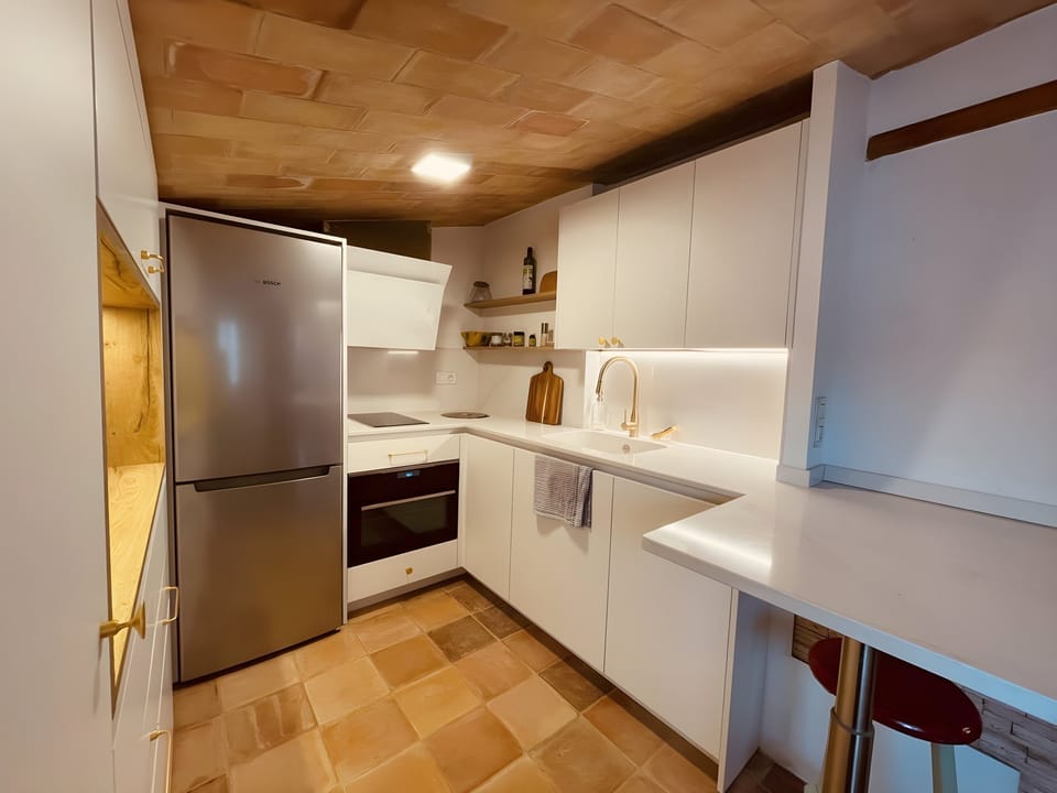 The modern kitchen boasts sleek white cabinetry, stainless steel appliances, and a stylish gold faucet. The exposed brick ceiling adds a touch of rustic charm, while the tiled floor provides a warm and inviting feel. There is plenty of counter space for p