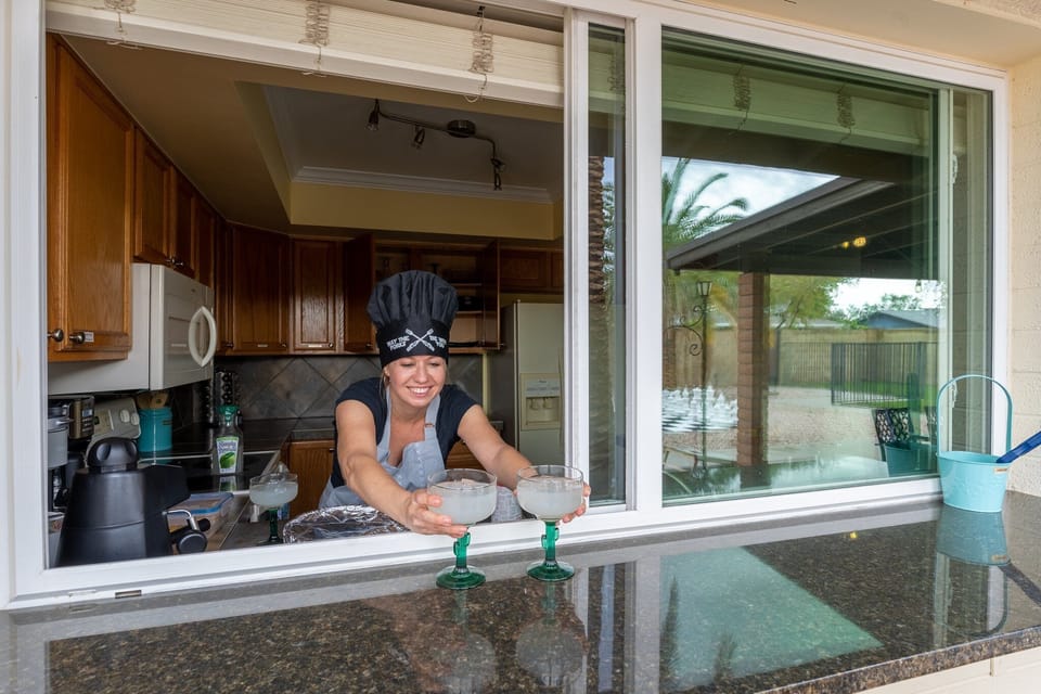 Kitchen window opens up to a counter top by the grill and patio dinner table