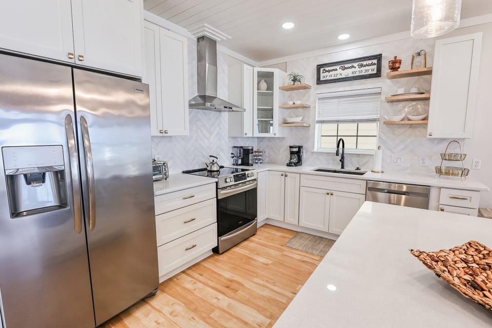 Your fully equipped kitchen awaits with gleaming countertops, stainless appliances, and open shelving displaying charming coastal touches for memorable meal prep.