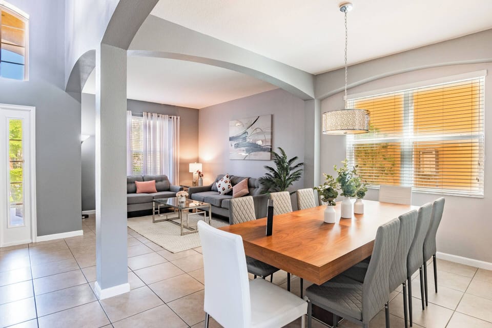 Enjoy our inviting dining area with a warm wooden table and soft chairs, ideal for meals with family and friends. Large windows let in natural light, enhancing the serene gray walls and tasteful decor for a perfect atmosphere.