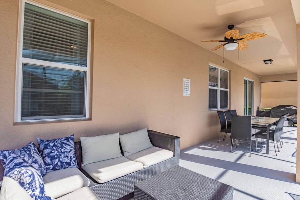 Enjoy the spacious patio with its comfortable seating and vibrant blue cushions. A ceiling fan provides a gentle breeze, and the dining table is perfect for savoring meals outdoors in the warm sunlight.