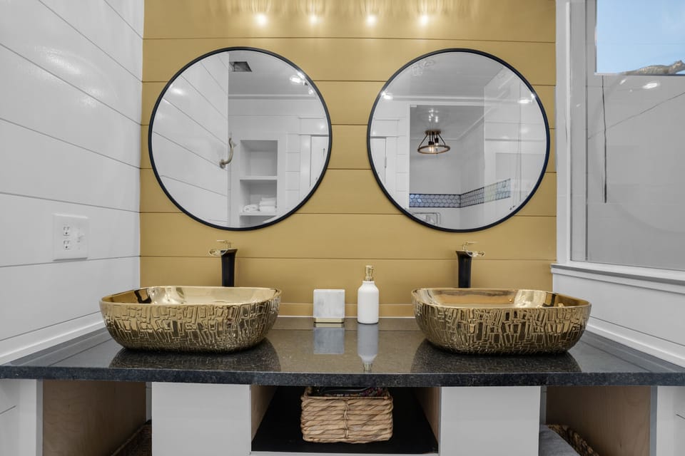 Pamper yourself in this stunning dual-sink bathroom with artistic vessel bowls, elegant gold accents, and thoughtful amenities for your daily routine.