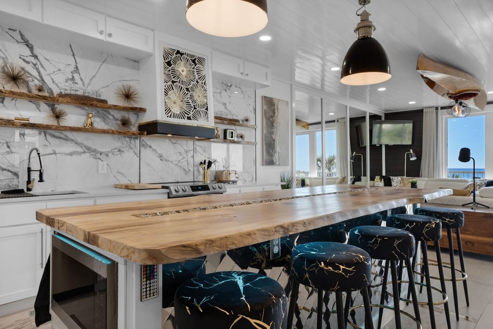 Your gourmet kitchen features a stunning live-edge wood island perfect for cooking together, with marble backsplash and ocean views.