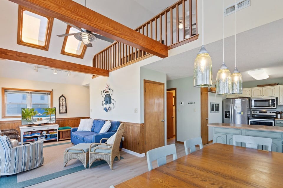 The bright and airy living area features large windows, comfortable seating, and a flat-screen TV, creating a welcoming space to unwind after a day in the sun.