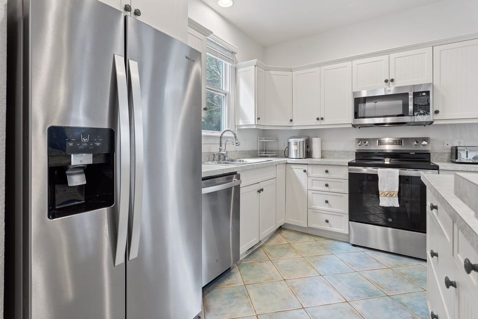 Bottom-Level Kitchen: Fully stocked kitchen with white cabinets, modern appliances, and ample counter space for preparing OBX favorites.
