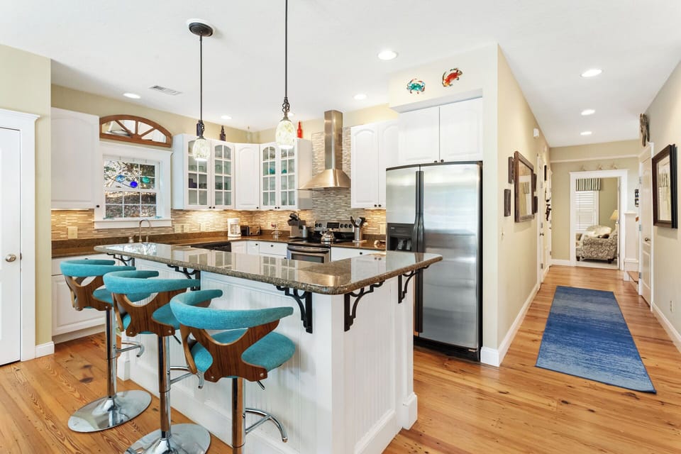 In the kitchen, you'll find additional bar seating for 3, as well as sleek stainless steel appliances and white cabinets with open glass doors.