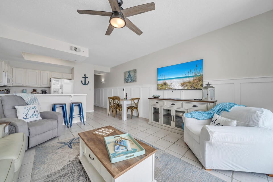 Relax in your coastal-themed living space with comfortable seating, beach artwork, and an open layout connecting to the fully equipped kitchen.