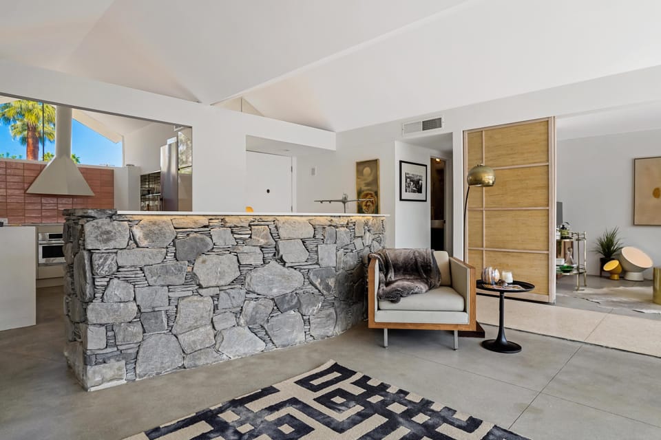 In the living room, there is a stone wall that has seating on the other side with bar stools.