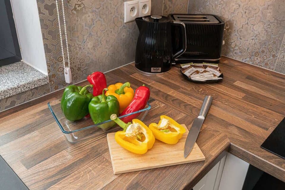 A neat countertop with a coffee maker, fresh vegetables, and a wooden cutting board, ready for meal prep.
