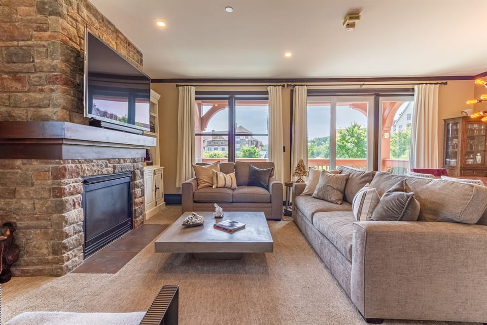 - Cozy mountain-view living room with wide windows showcasing scenic resort views - Stone fireplace, plush sofas, and warm lodge decor create relaxing comfort - Ideal retreat for après-ski lounging and mountain getaways