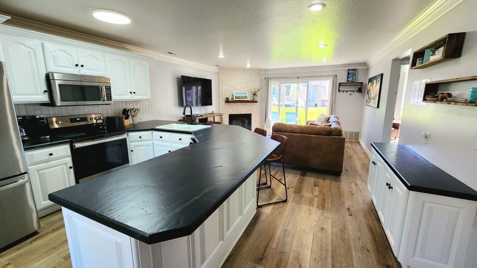Open-concept kitchen and living area with island seating, fireplace, and bright patio access for relaxing stays