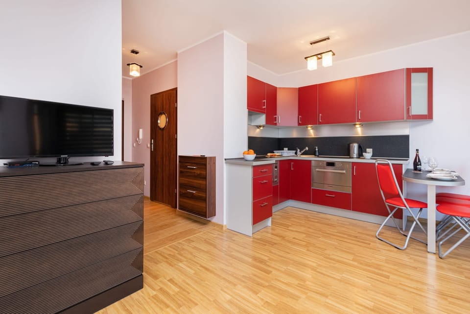Open-plan view of the living area leading into a red kitchen with functional modern design.
