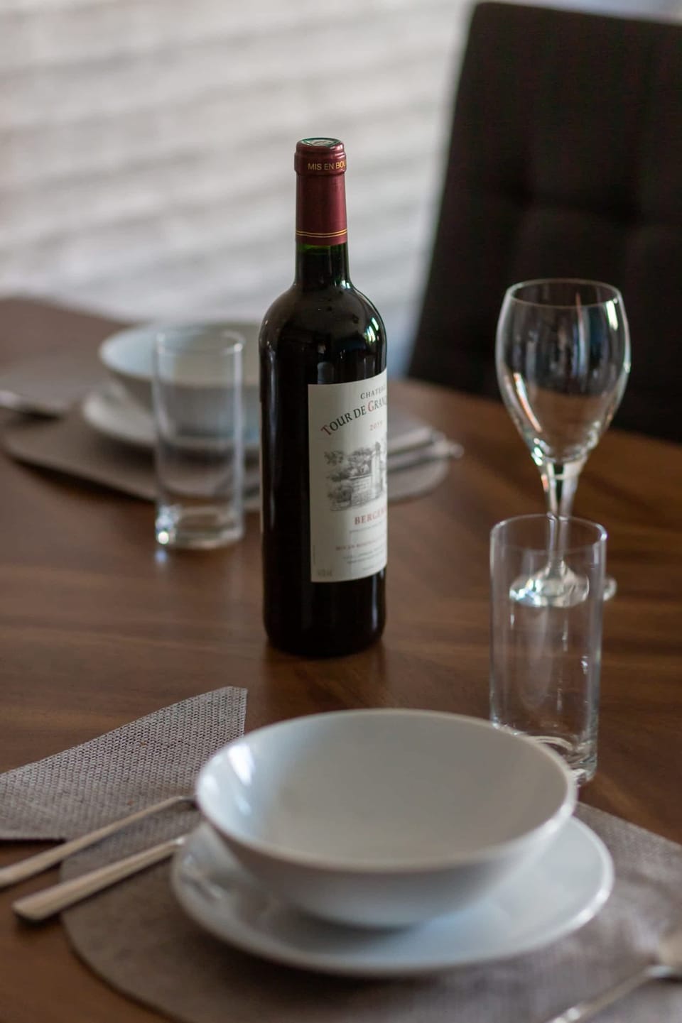 A wooden table set with wine glasses, a bottle of wine, and a minimalist aesthetic.