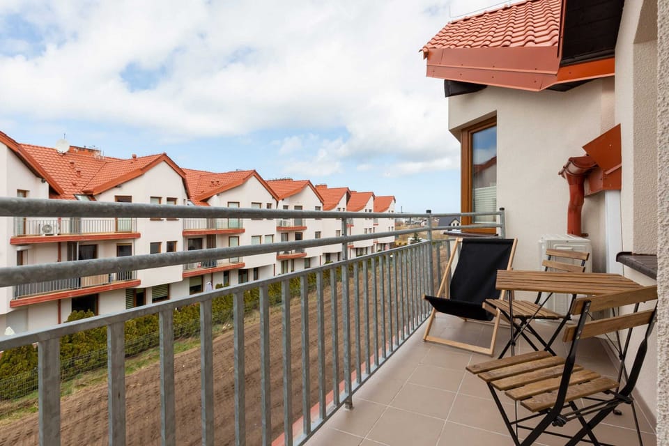 A cozy balcony with two chairs and a table, overlooking the rooftops of nearby buildings.