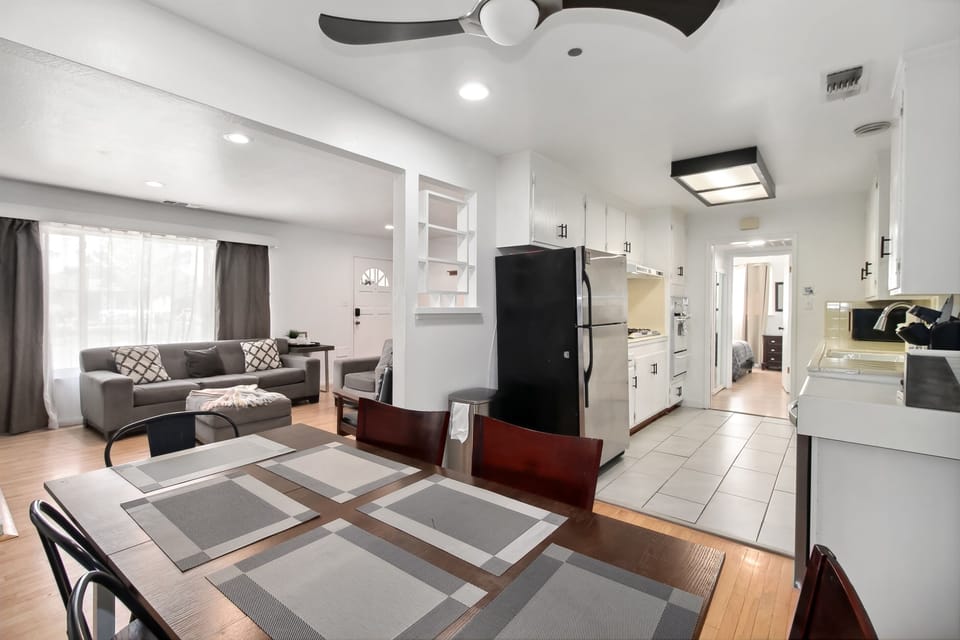 "Elegant dining area with seating for six, featuring a modern ceiling fan and large wall art of a waterfall. French doors bring in natural light, adding to the room's inviting ambiance."