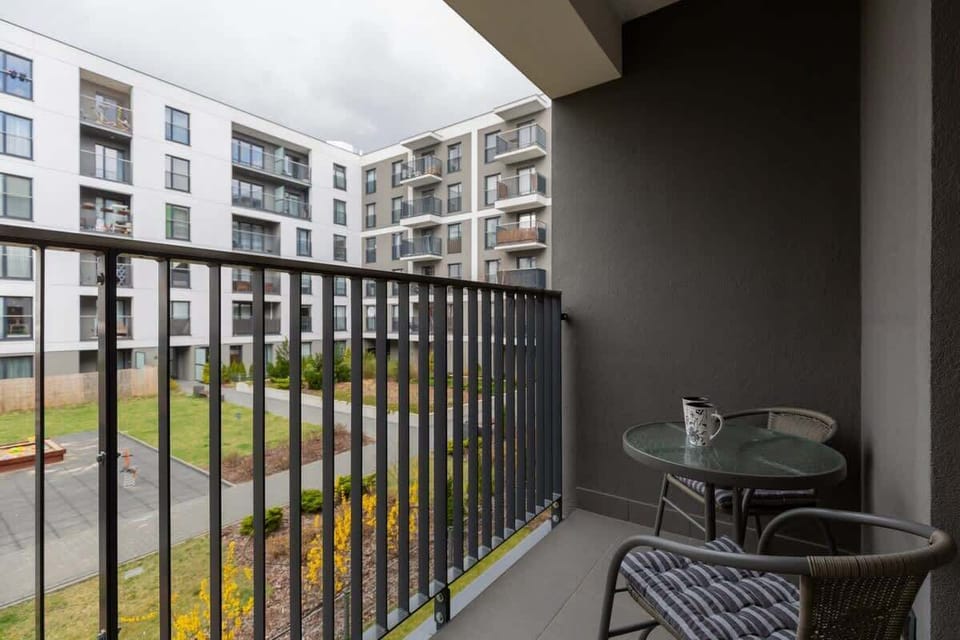 A balcony area with a view of an outdoor courtyard and neighboring buildings. Railings and a small table are visible.