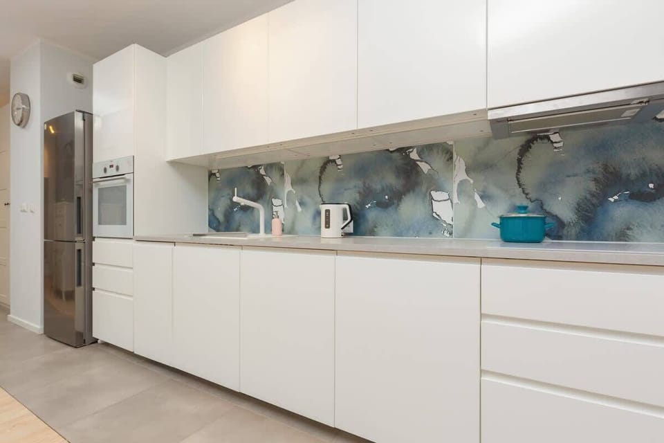 A sleek kitchen with white cabinets and a modern backsplash showcasing a creative, glass-style design. Countertops are clean, and small appliances are visible.