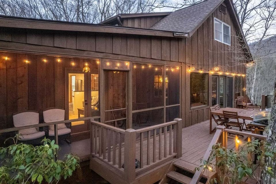Evening view of the screened-in porch and expansive deck with festive string lighting at this Baines Mountain cabin.